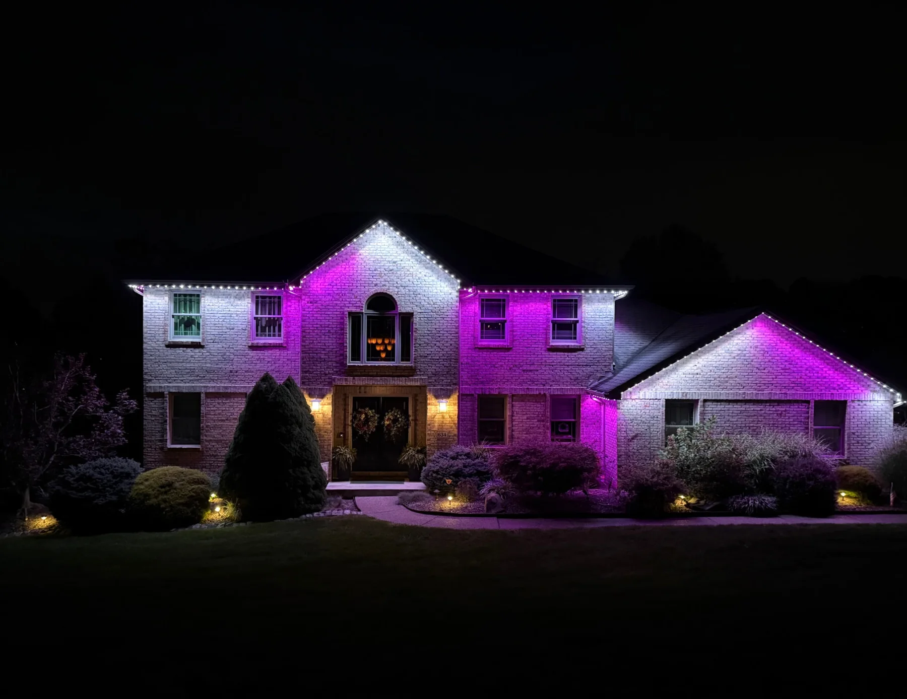 White and purple permanent roofline lighting on a two-story brick home