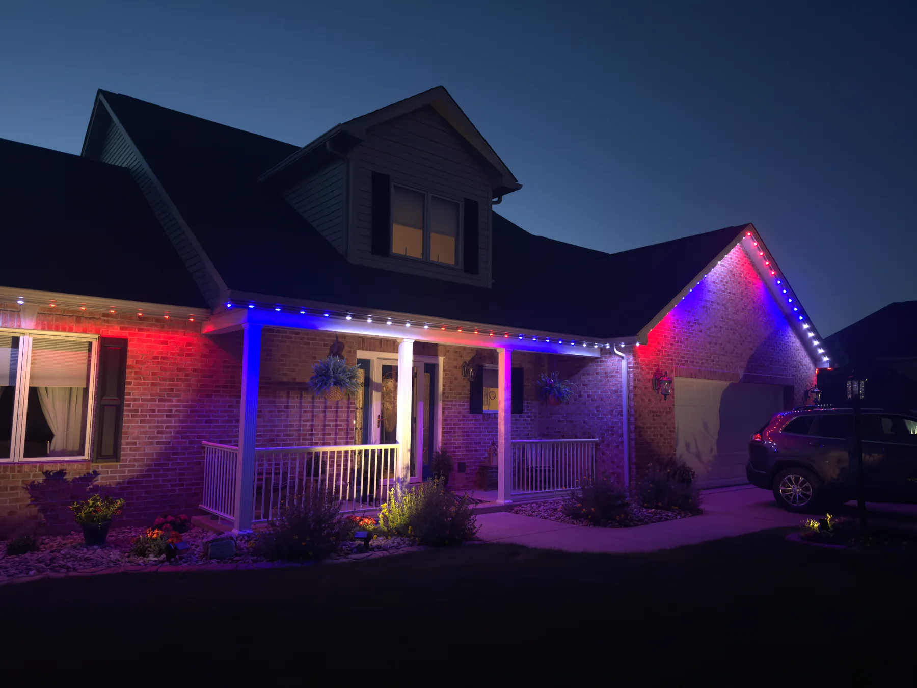 Patriotic permanent roofline lighting on a brick home at dusk