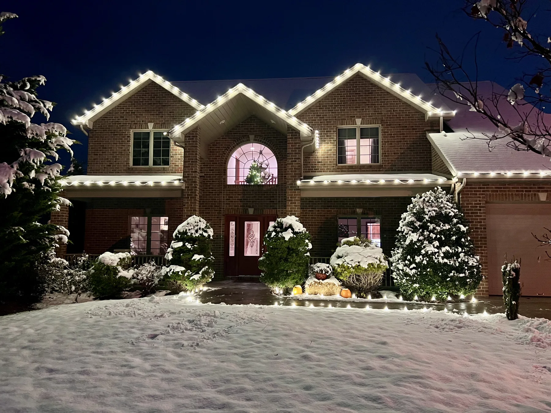 Warm white Christmas roofline lighting on a snow-covered brick home