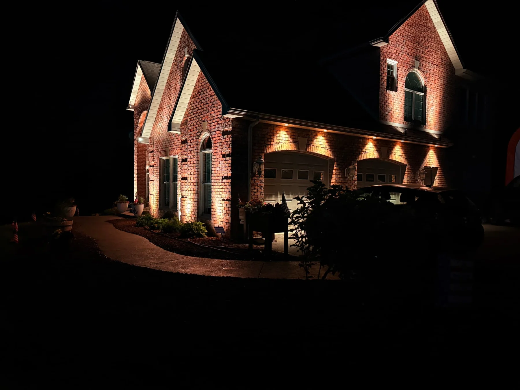 Warm architectural uplighting across a brick home and garage